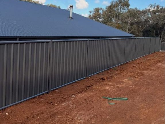 Long grey Colorbond fence along a new build
