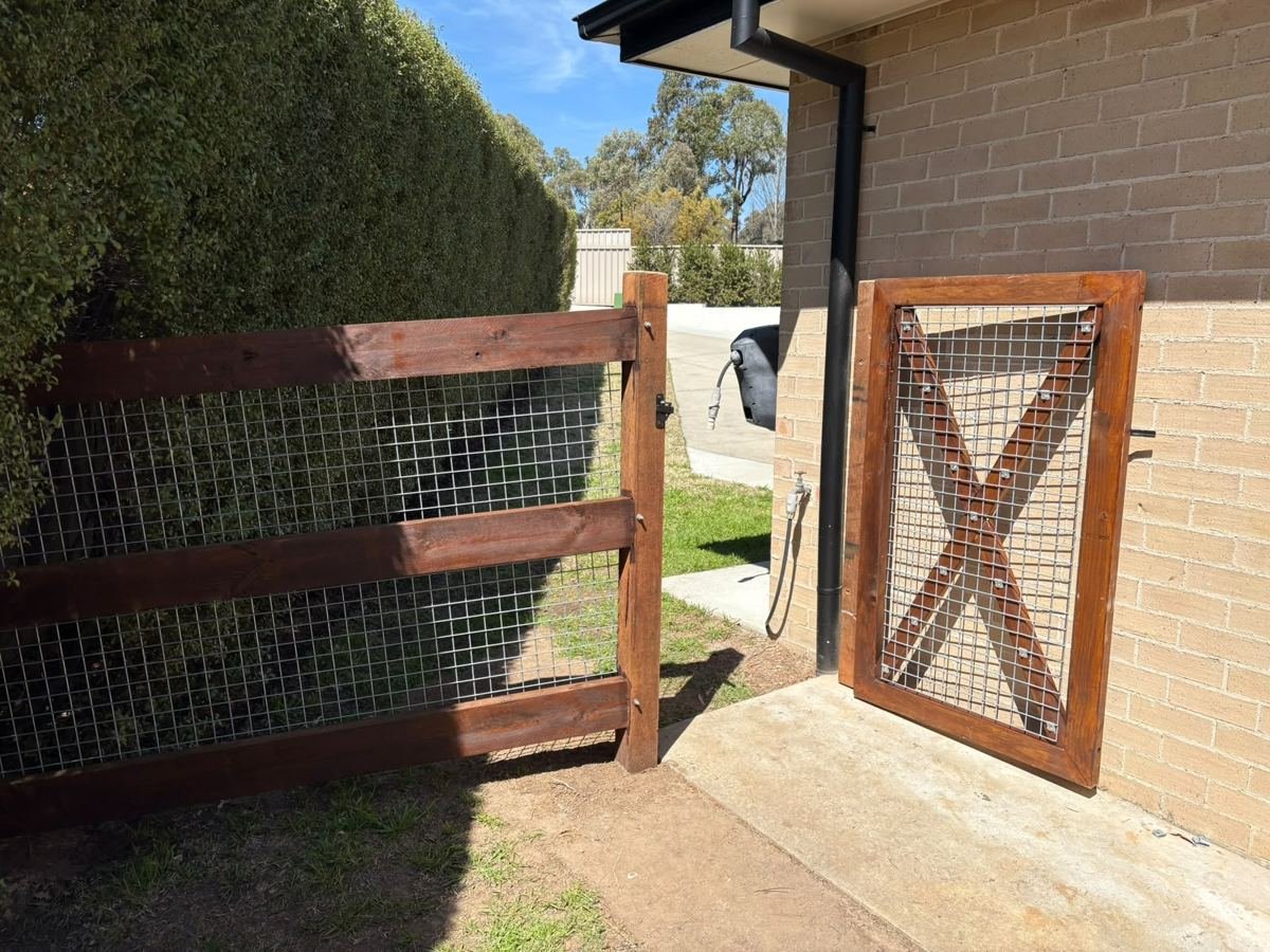 Hardwood post and rail fence with mesh and a braced gate beside a brick home